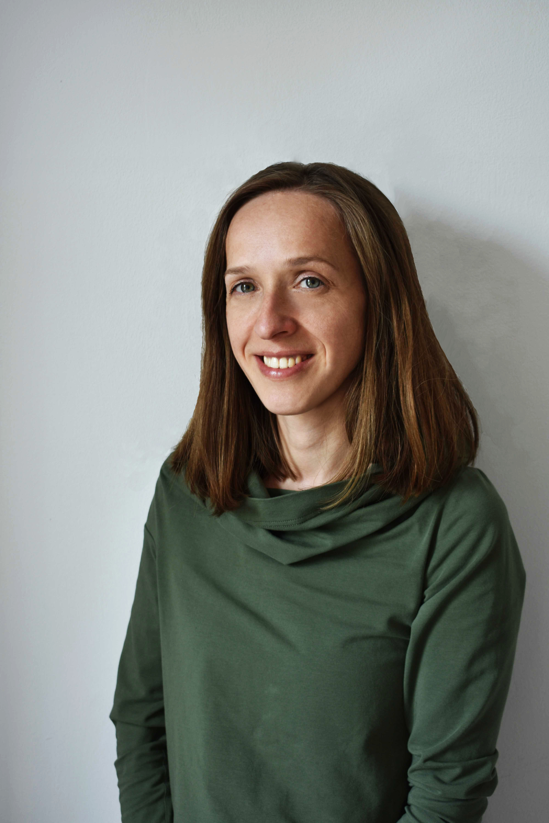 The women with brown hair. She is smiling. She wears green sweater.