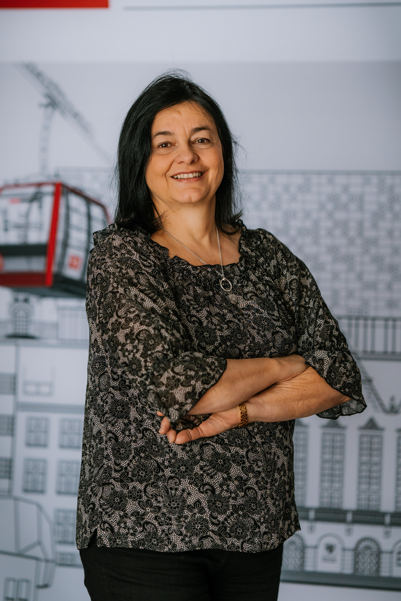 The above picture presents a smiling, middle-aged woman with shoulder-length dark  hair. She’s wearing  a black and white, patterned lace blouse.