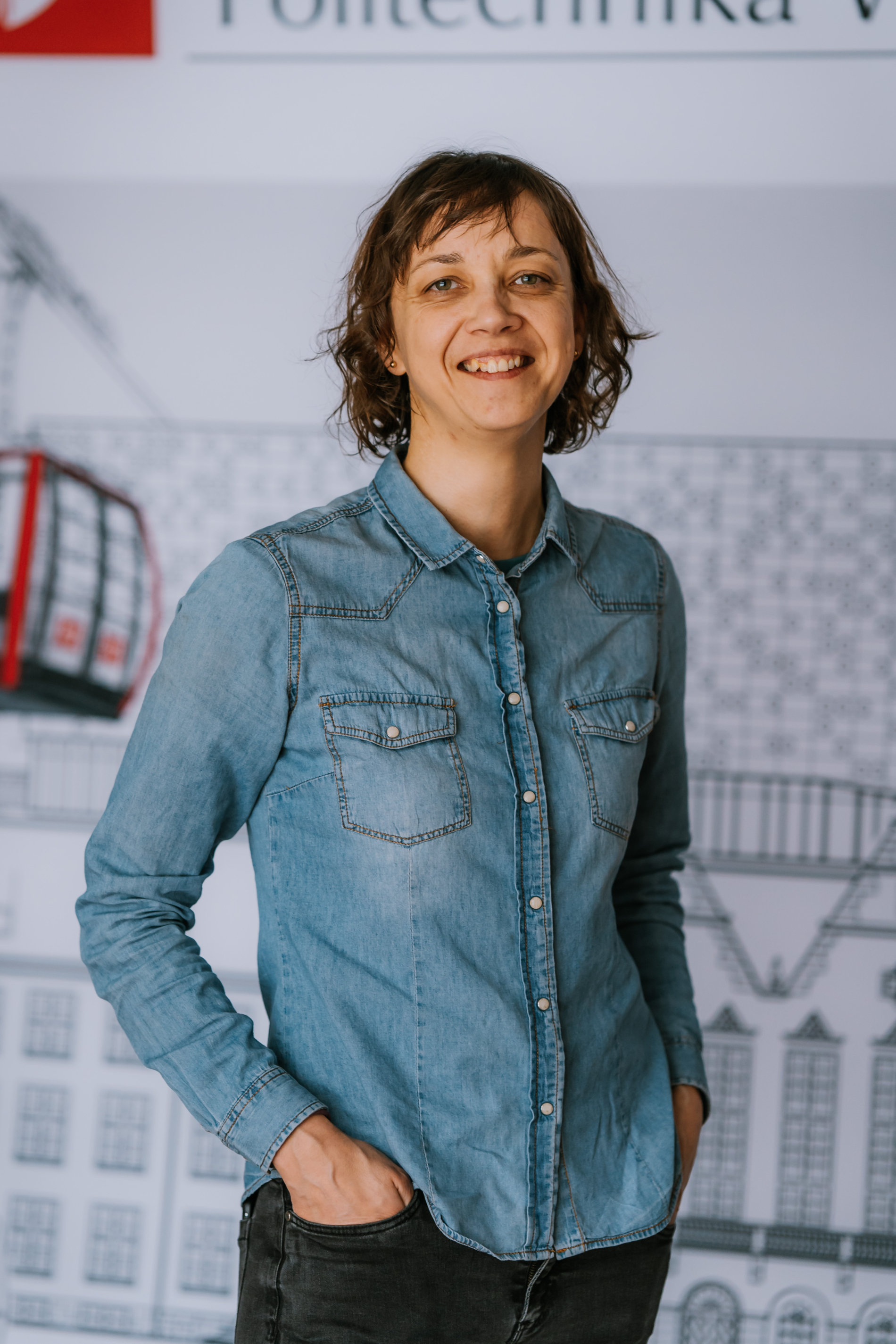 Smiling women with braun hair. She is wearing blue jacket and jeans.