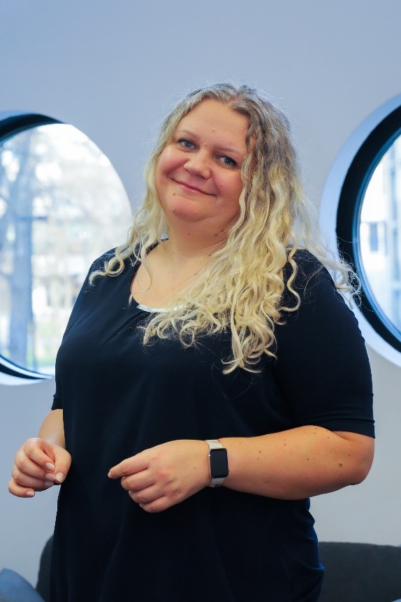 Smiling women with curly, blond hair. She is wearing black dress.